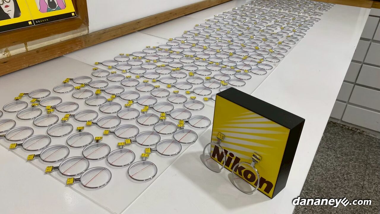 桌面上一排排做好的 Nikon 原廠單片試戴鏡片，旁邊立著 Nikon 燈箱示意